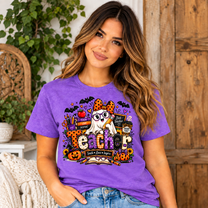 A woman wearing a purple graphic t-shirt with a Halloween-themed 'Teacher' design, posed in a cozy indoor setting with a wooden door and plants in the background.